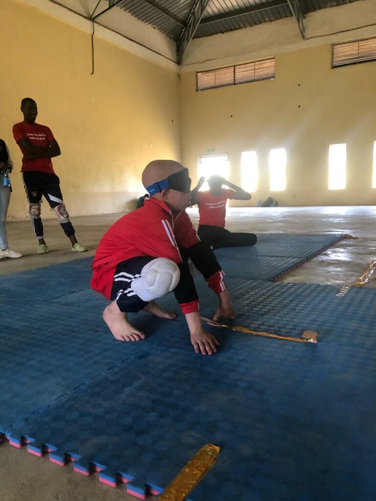 A child crouched down with a blindfold and kneepads practicing goal ball.